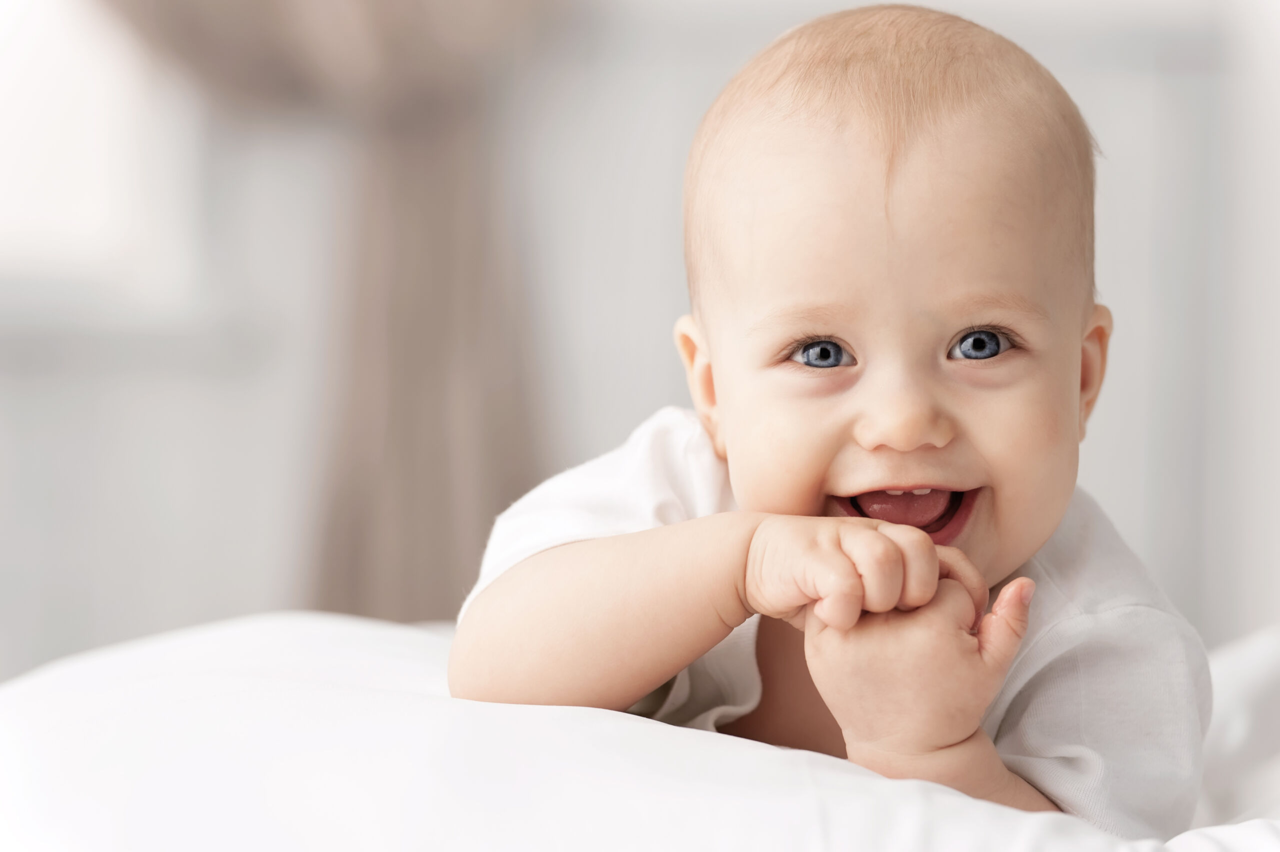 ein lachendes Baby legt auf dem Bauch auf einem Kissen und hält die Hände an den Mund